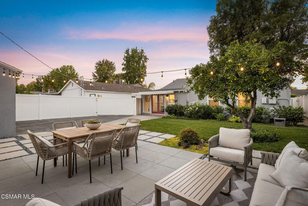 Backyard patio with outdoor dining and lounge furniture, lawn, mature tree, and string lights at dusk.