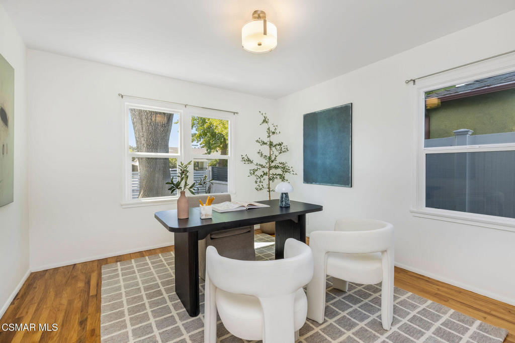 Staged home office with a black desk, white chairs, and windows overlooking a tree.