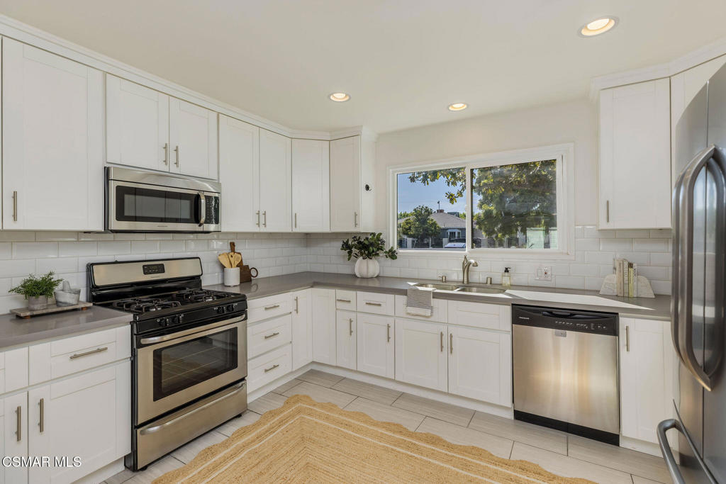 Bright white kitchen with stainless steel appliances and a window above the sink.