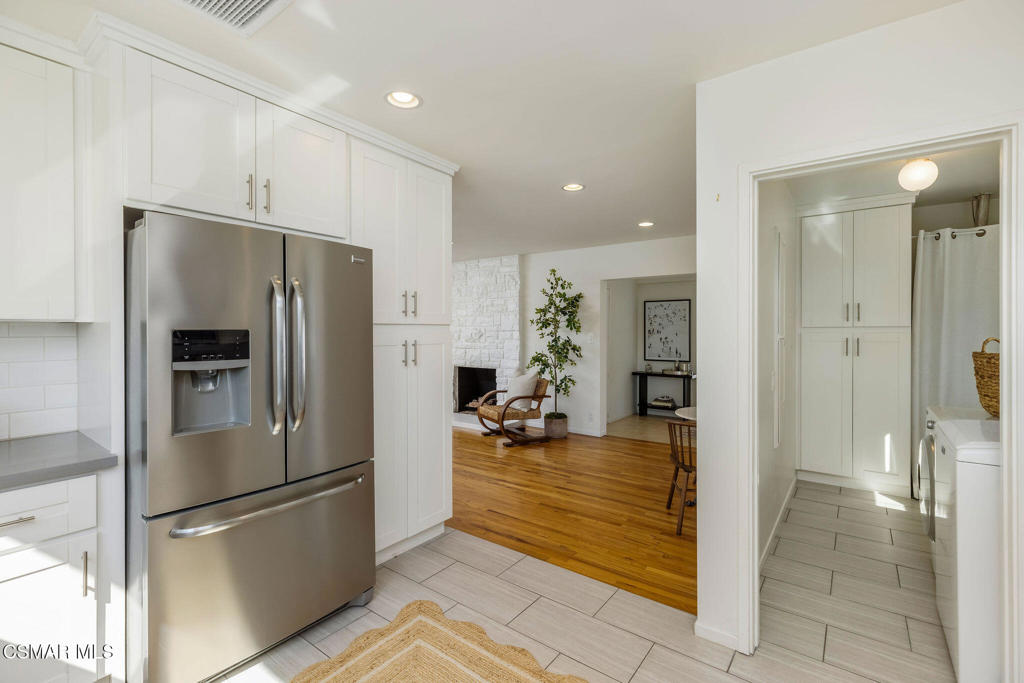 White kitchen with stainless-steel refrigerator, opening to a living area and laundry room.