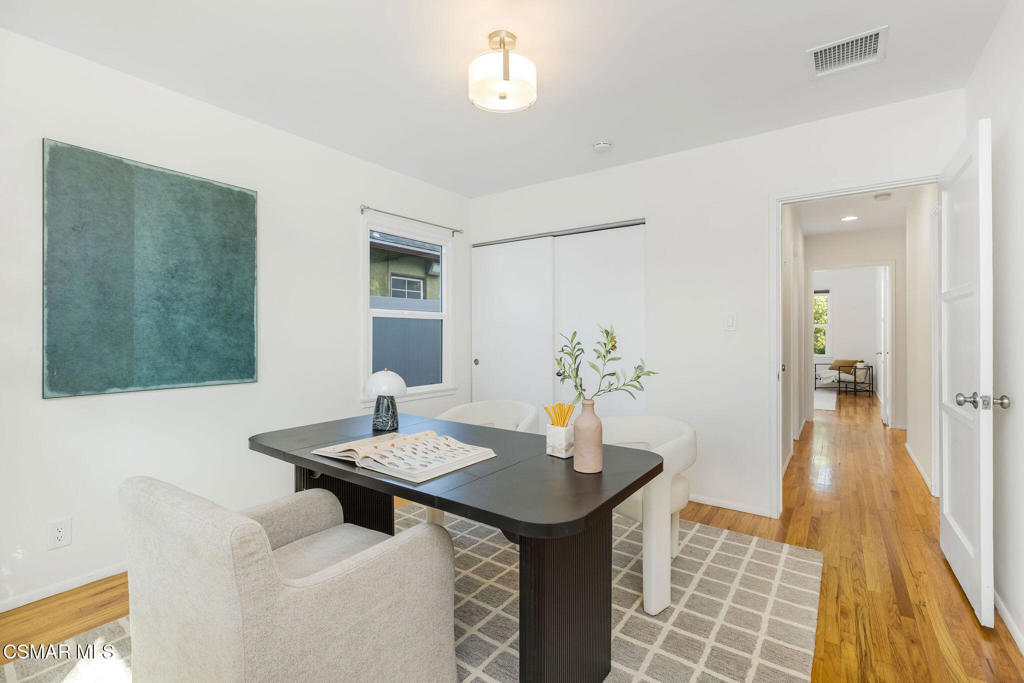 Staged home office with a dark desk, cream chairs, and a hallway beyond.