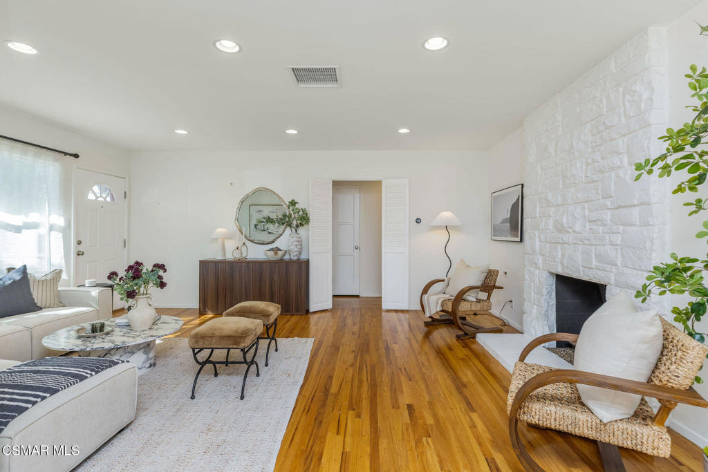 Living room with hardwood floors, a white stone fireplace, and neutral seating.