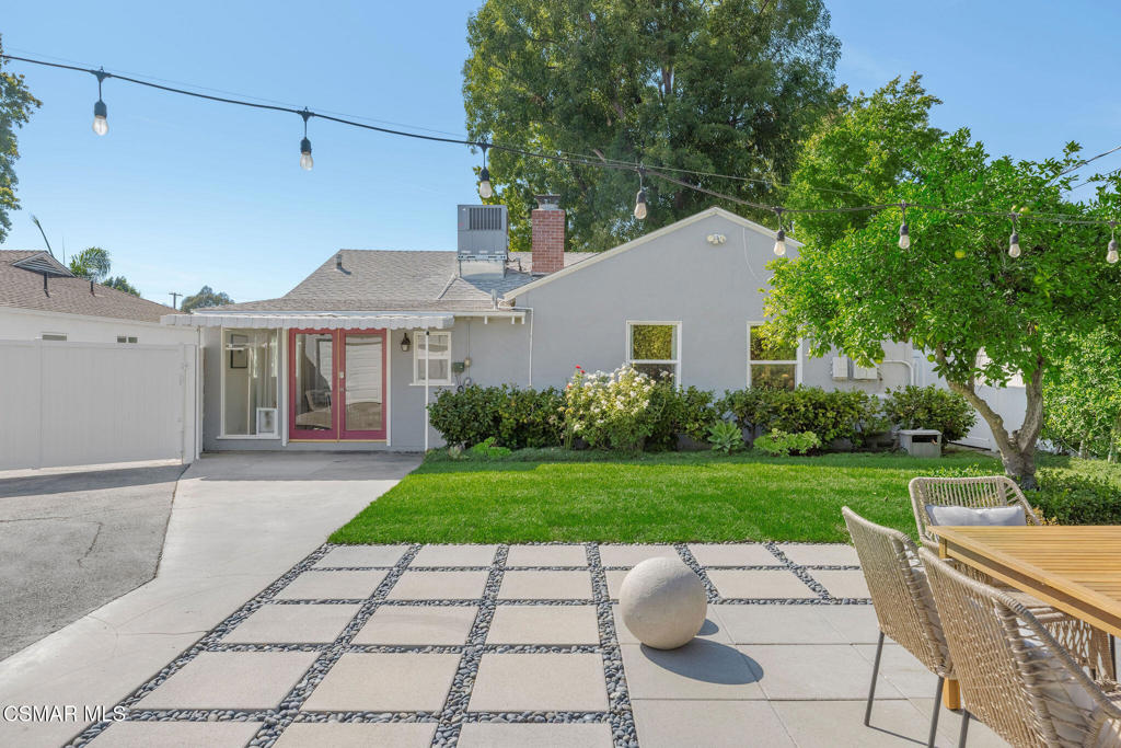 Backyard patio with lawn, outdoor dining furniture, and string lights beside a gray single-story home.