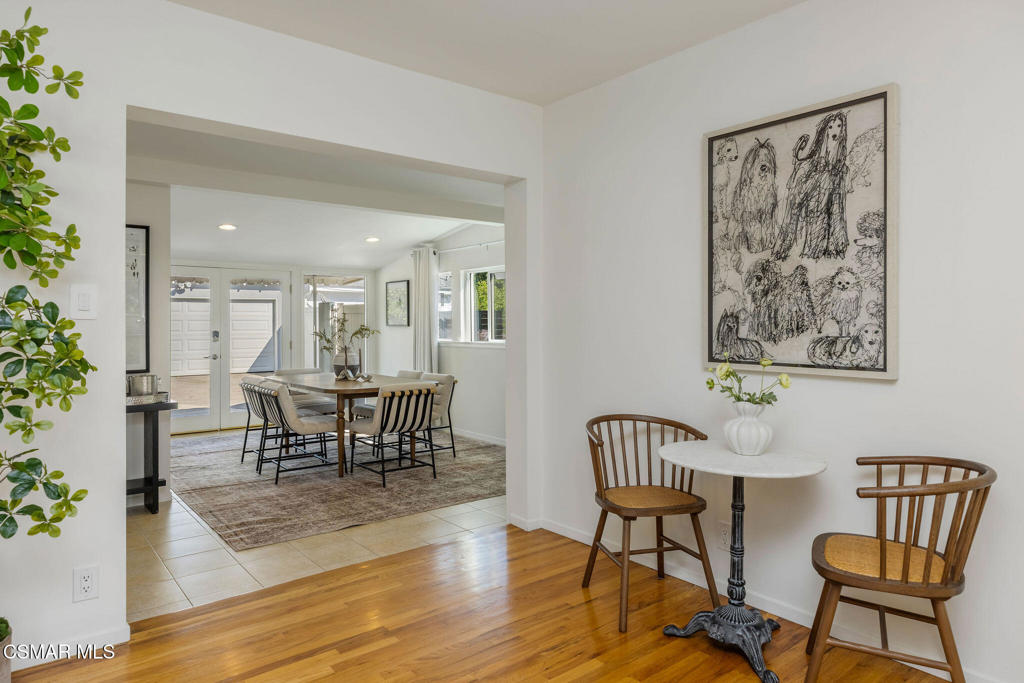 Dining area with a small round table and wooden chairs, opening to a larger dining room with glass doors.