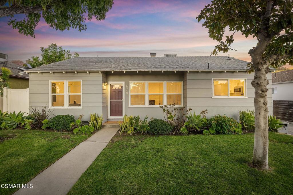Single-story gray home with a landscaped front lawn, concrete walkway, and mature trees at dusk.