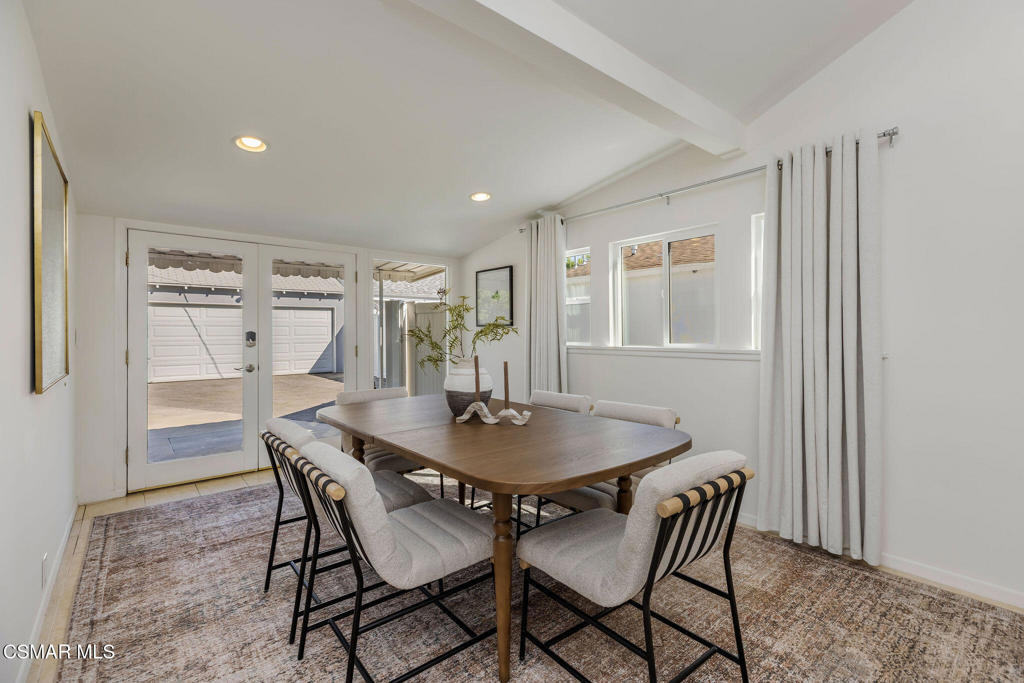Dining room with a wood table, upholstered chairs, and glass doors opening toward the driveway.