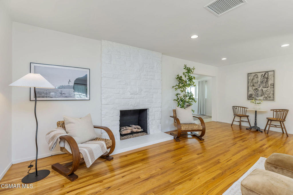 Living room with a white stone fireplace, curved wooden chairs, and hardwood floors.