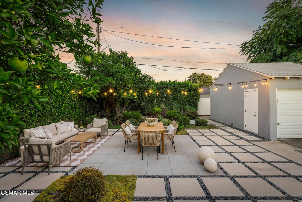 Backyard patio with lounge seating, a dining table, and glowing string lights at dusk.