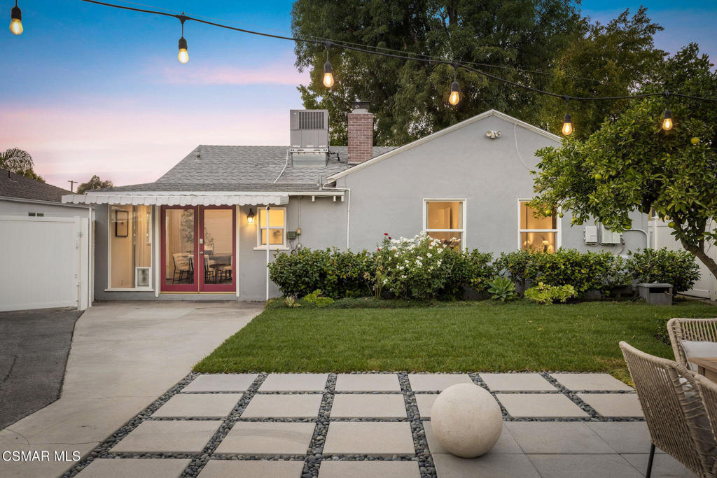 Home’s rear exterior at dusk, with string lights above a lawn and geometric stone patio.