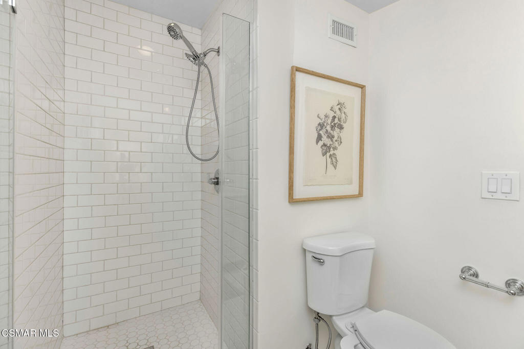 Bathroom with a white subway-tile walk-in shower, glass panel, and framed botanical print.