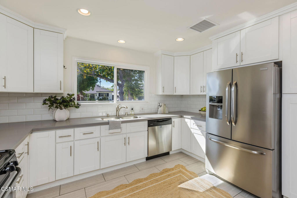 Bright kitchen with white cabinets, stainless steel appliances, and a window overlooking leafy trees.
