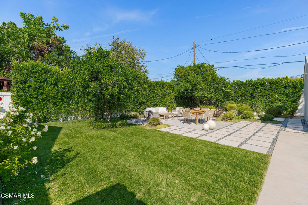 Backyard with a broad lawn and a paved patio furnished with outdoor seating and a dining table.