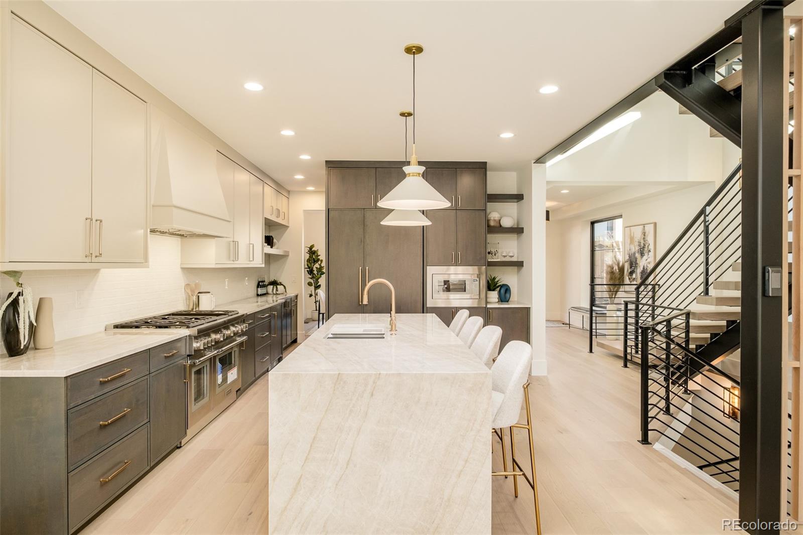 Modern kitchen with a large marble island, dark cabinetry, and an adjacent black metal staircase.