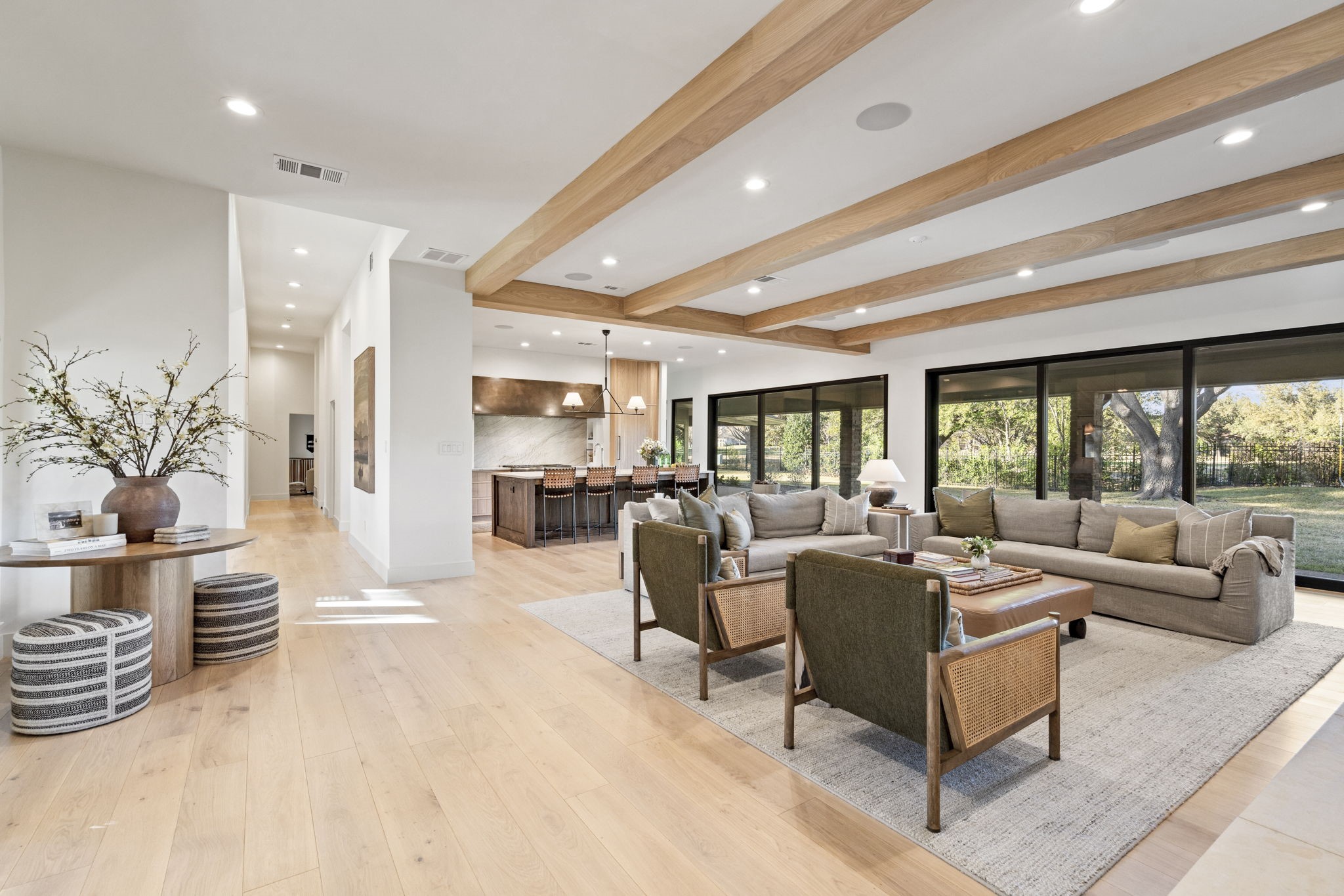 Open-plan living room with exposed wood beams, large windows, and a kitchen island.