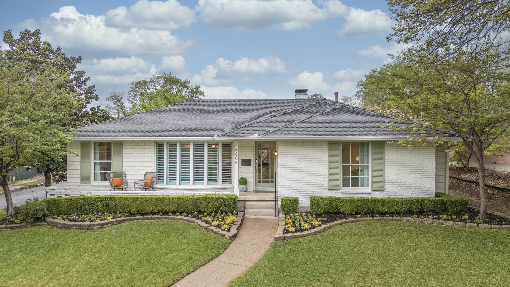 White brick ranch home with pale green shutters, landscaped lawn, and a curved front walkway.