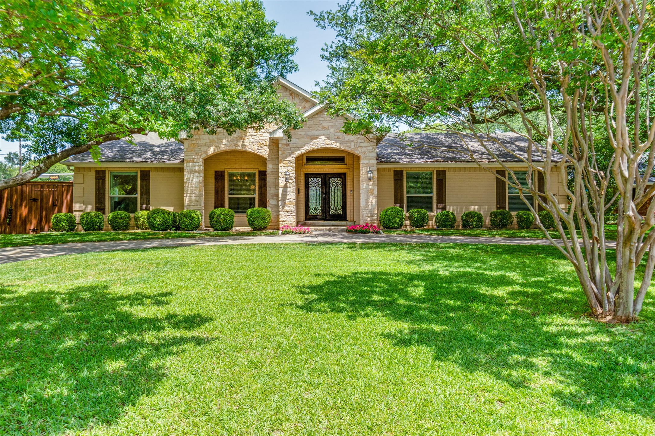 Single-story home with a stone entry, decorative double doors, and a shaded front lawn.