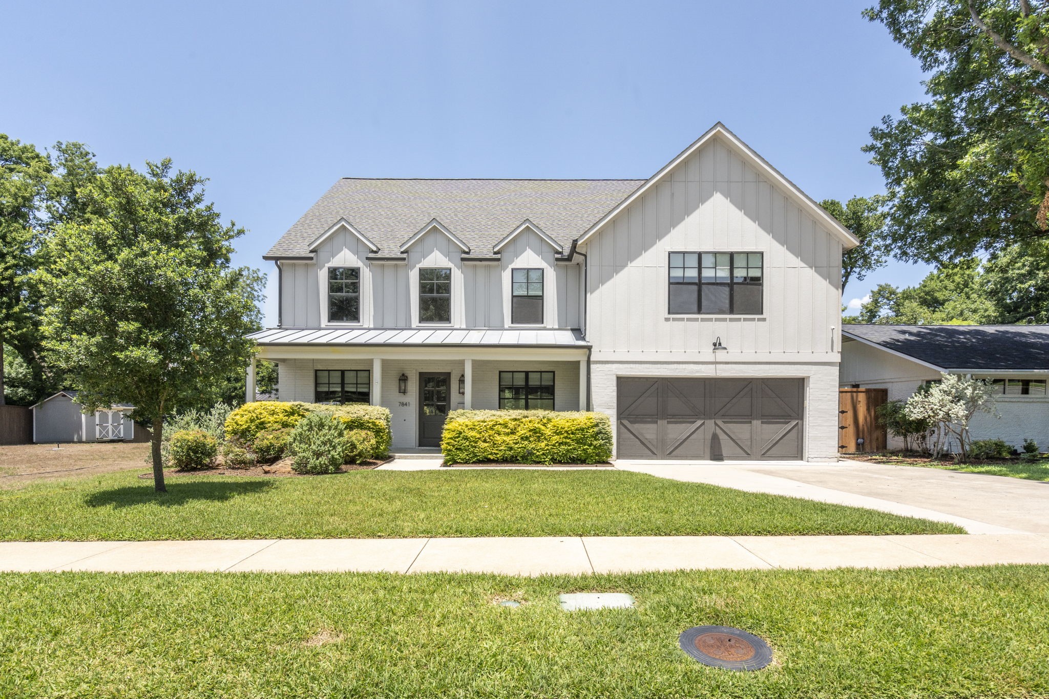 Two-story white house with a covered porch, dark double garage, and landscaped front lawn.