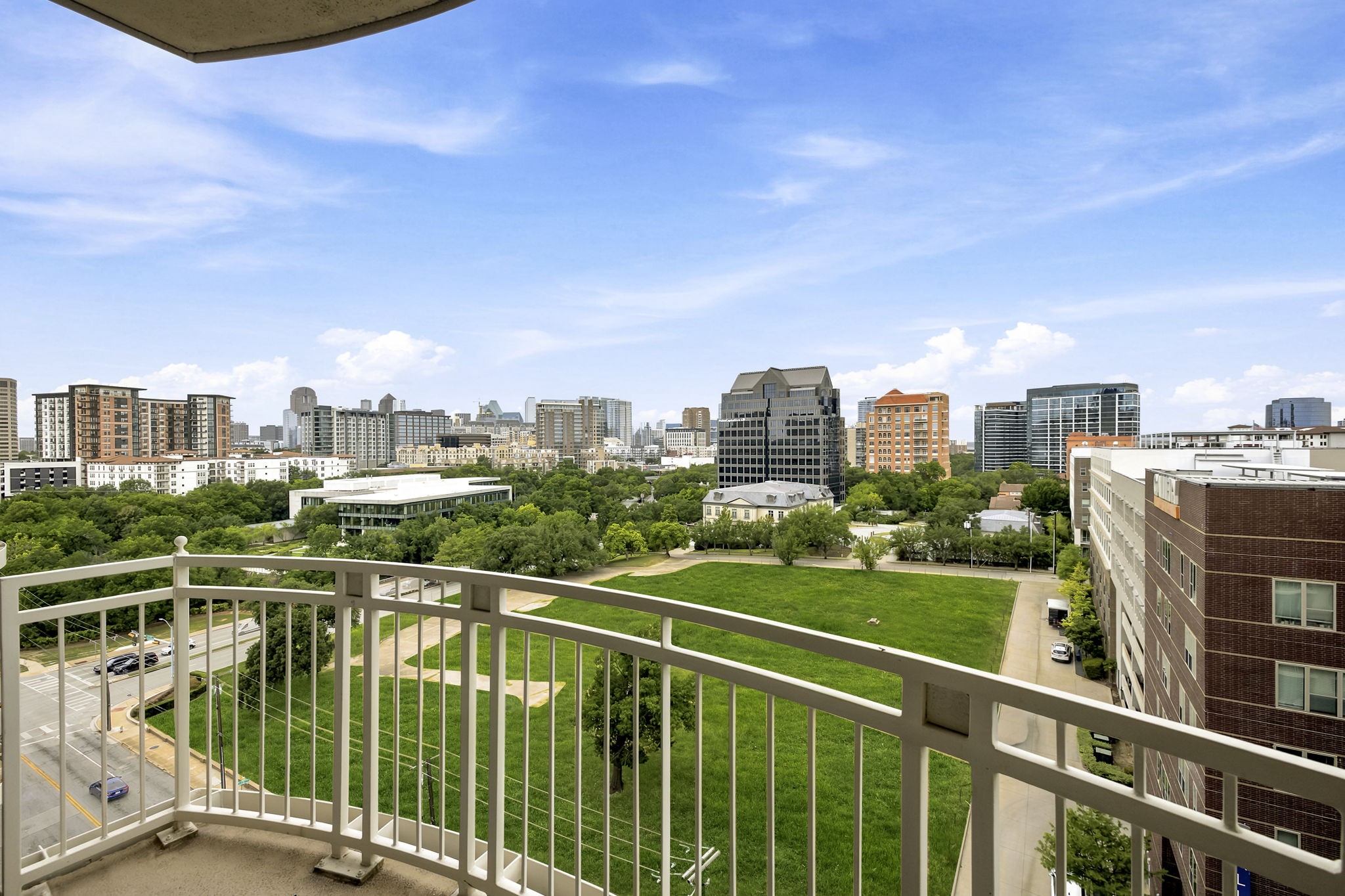 Balcony overlooking a green park and Dallas skyline, framed by a white railing.