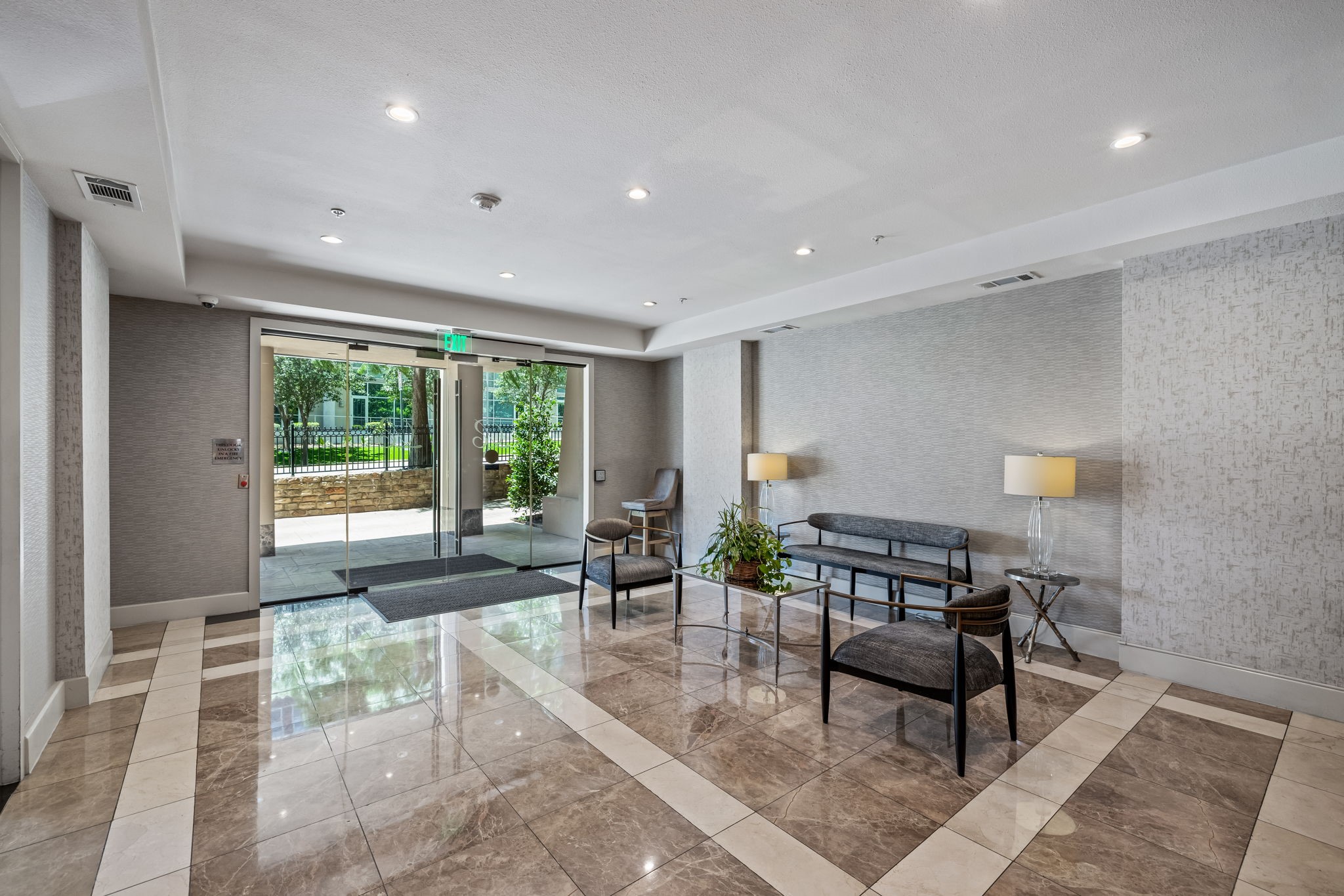 Condominium lobby with gray seating, glossy patterned tile, and glass entrance doors.