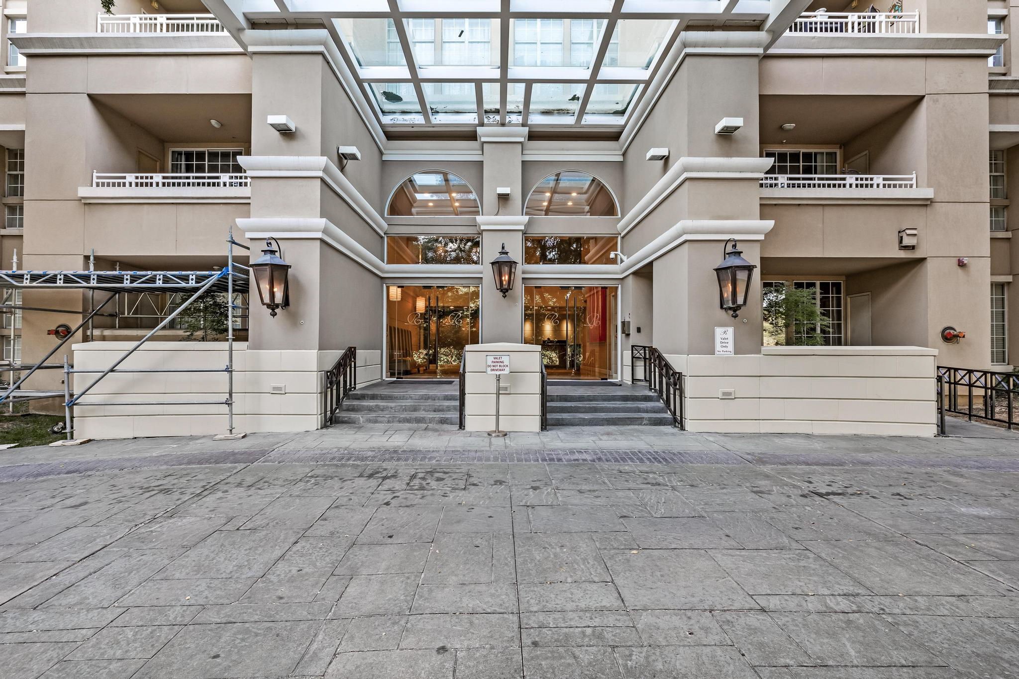 Condominium entrance beneath a glass canopy, with arched windows and scaffolding beside the steps.