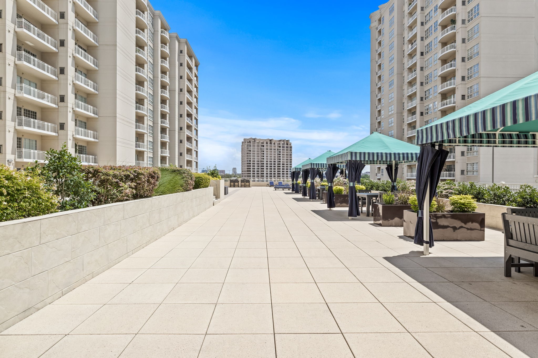 High-rise residential terrace with tiled paving, landscaped planters, and striped cabanas.