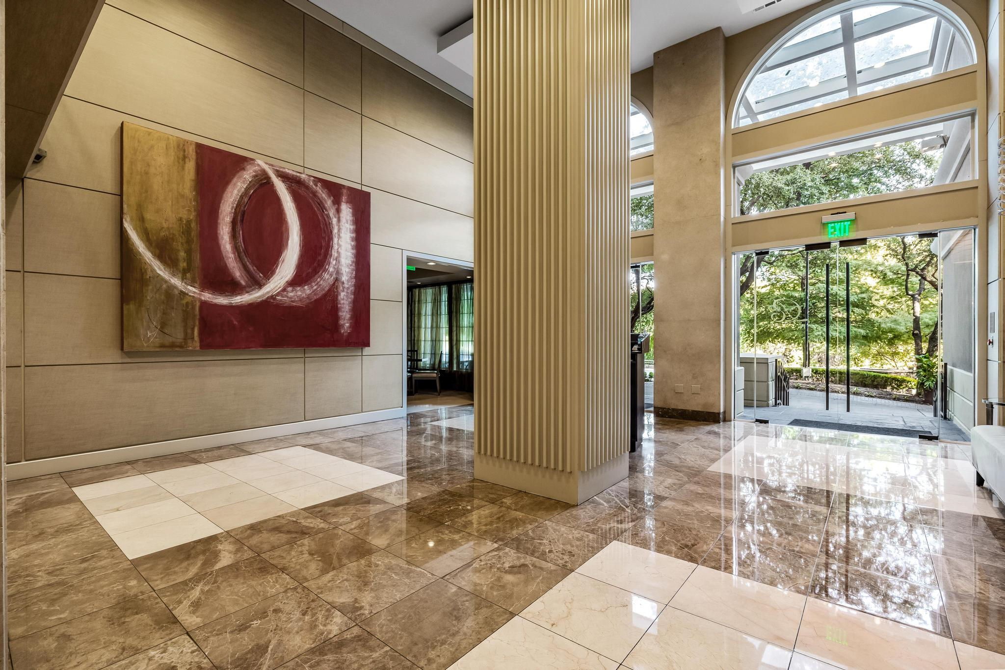 Condominium lobby with polished marble floors, a fluted column, abstract art, and arched glass entrance doors.