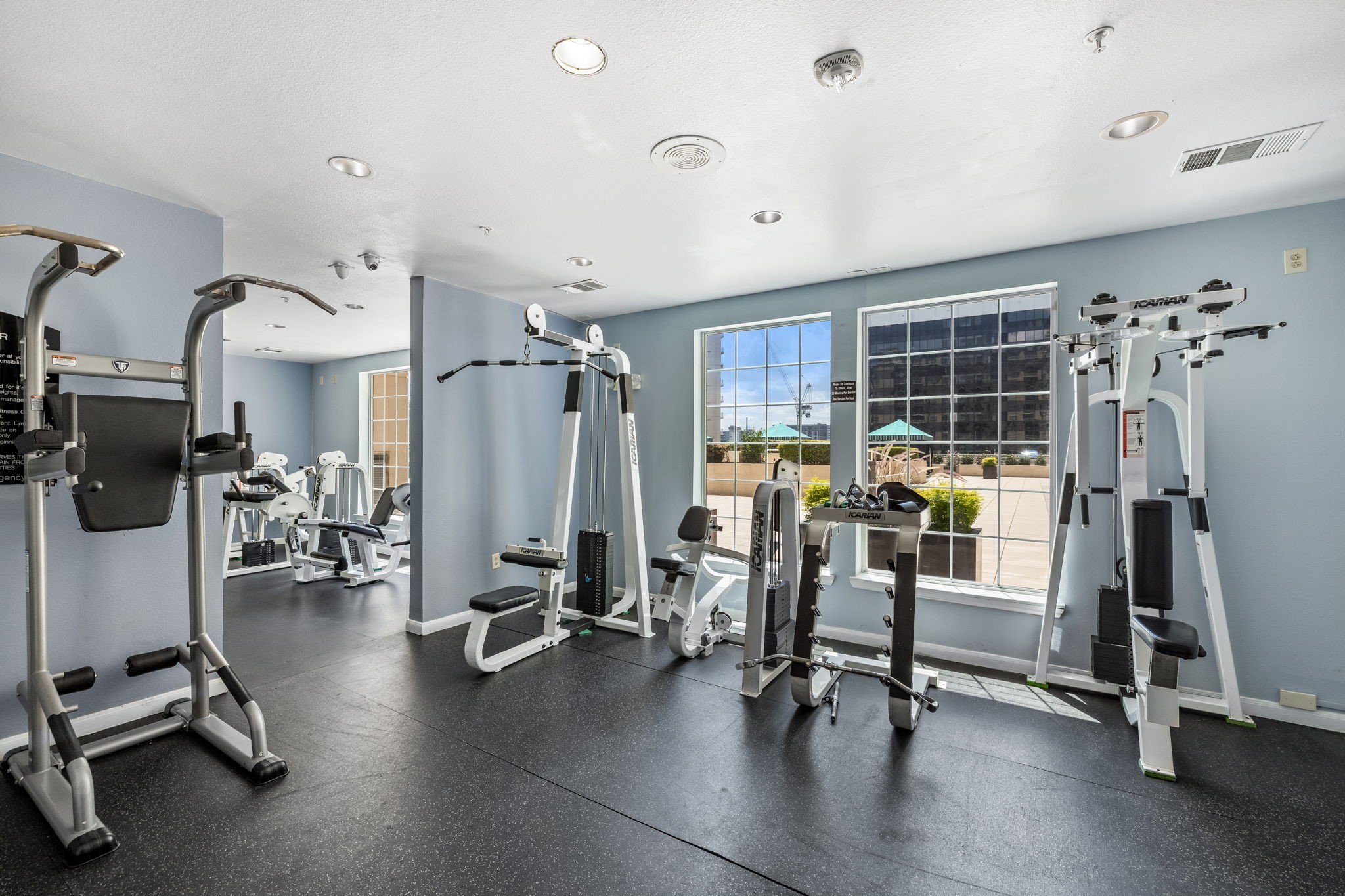 Condominium fitness room with weight machines, large windows, and a terrace view.