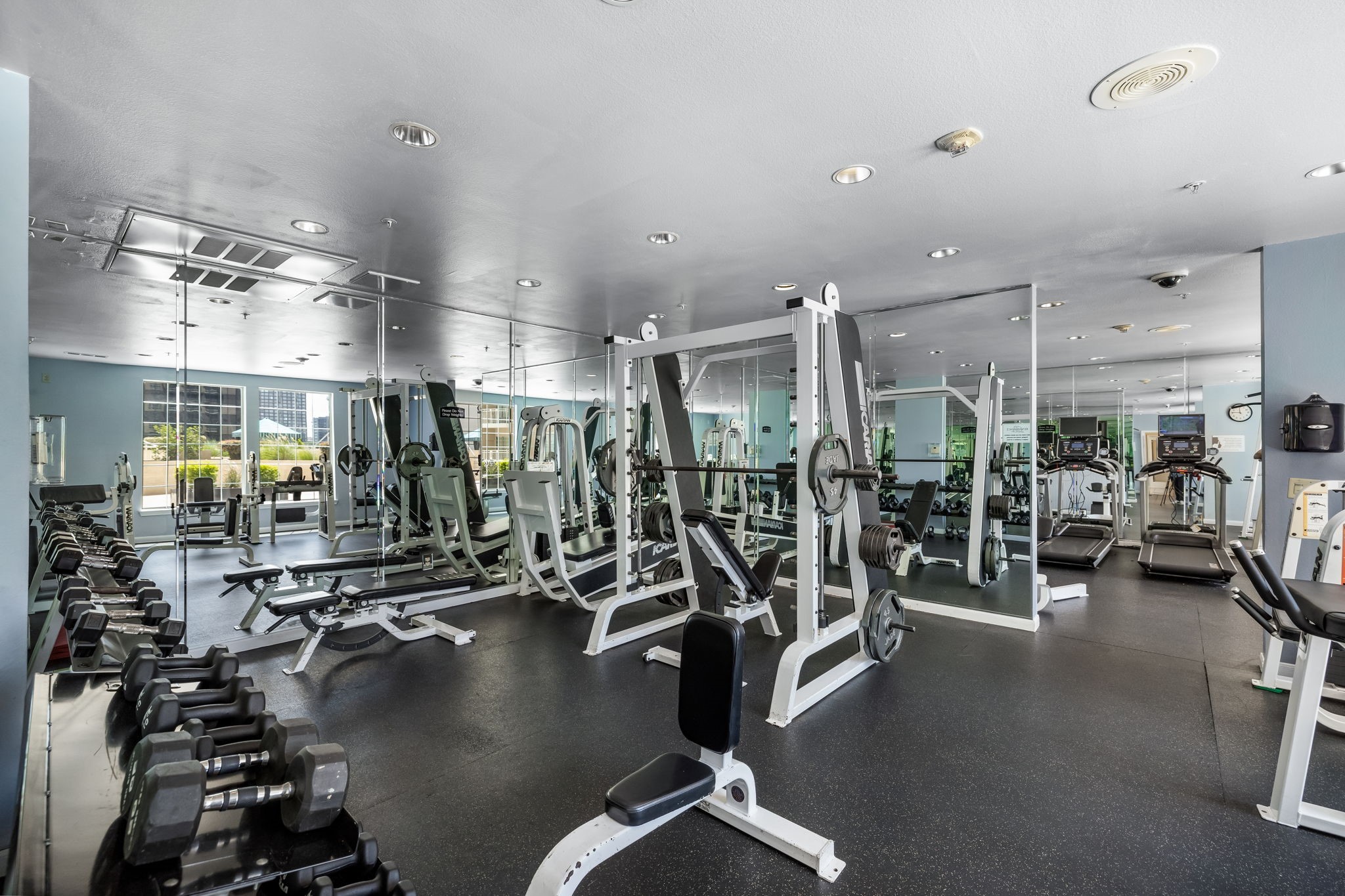 Fitness center with mirrored walls, weight machines, dumbbells, and treadmills.