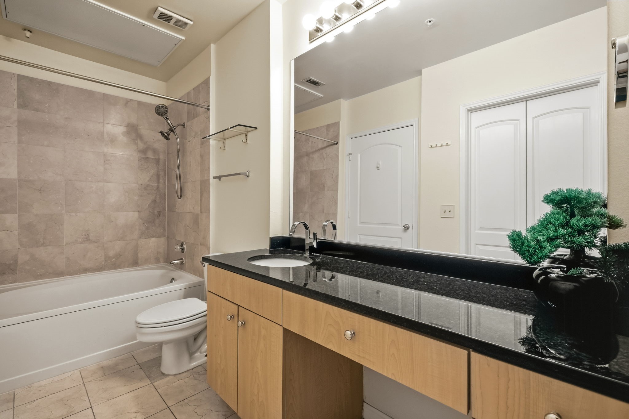 Bathroom with tiled tub and shower, toilet, and black stone vanity with wood cabinets.