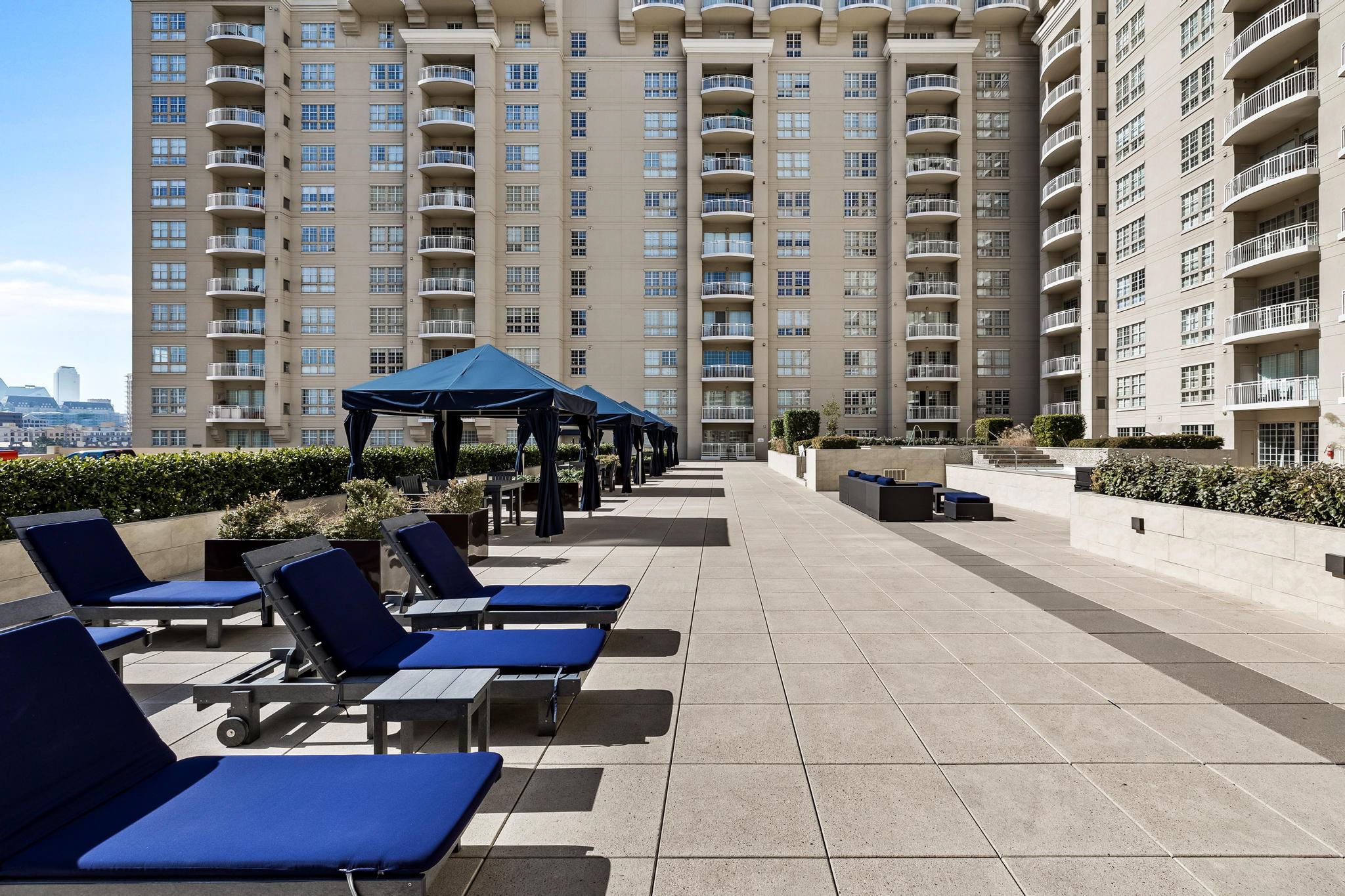 Condominium terrace with blue lounge chairs, navy cabanas, and surrounding high-rise buildings.