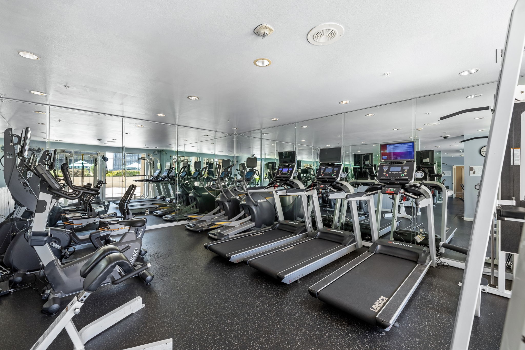 Condominium gym with rows of treadmills and ellipticals facing mirrored walls.