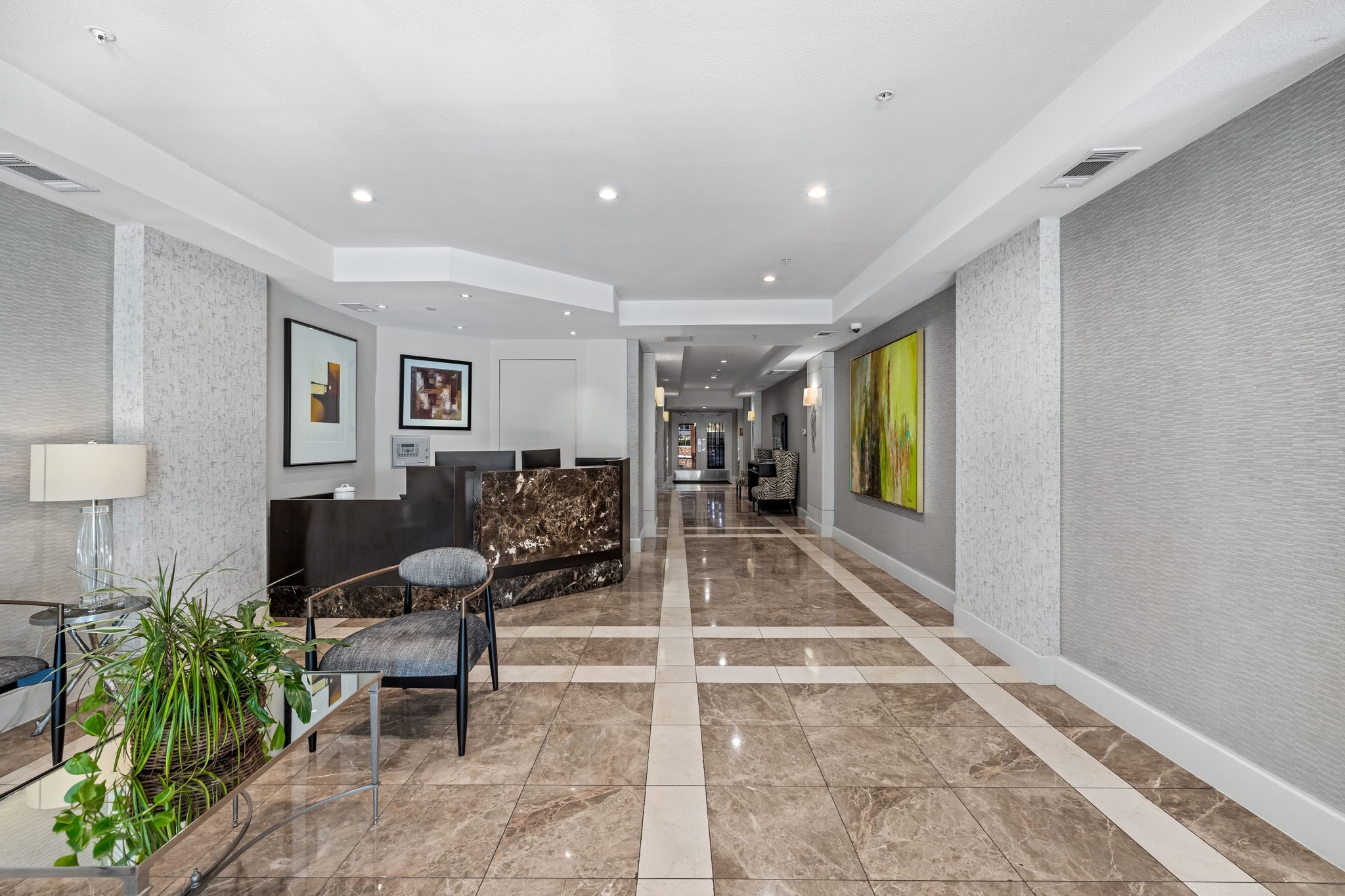 Condominium lobby with a marble reception desk, polished tile floors, artwork, and seating with plants.