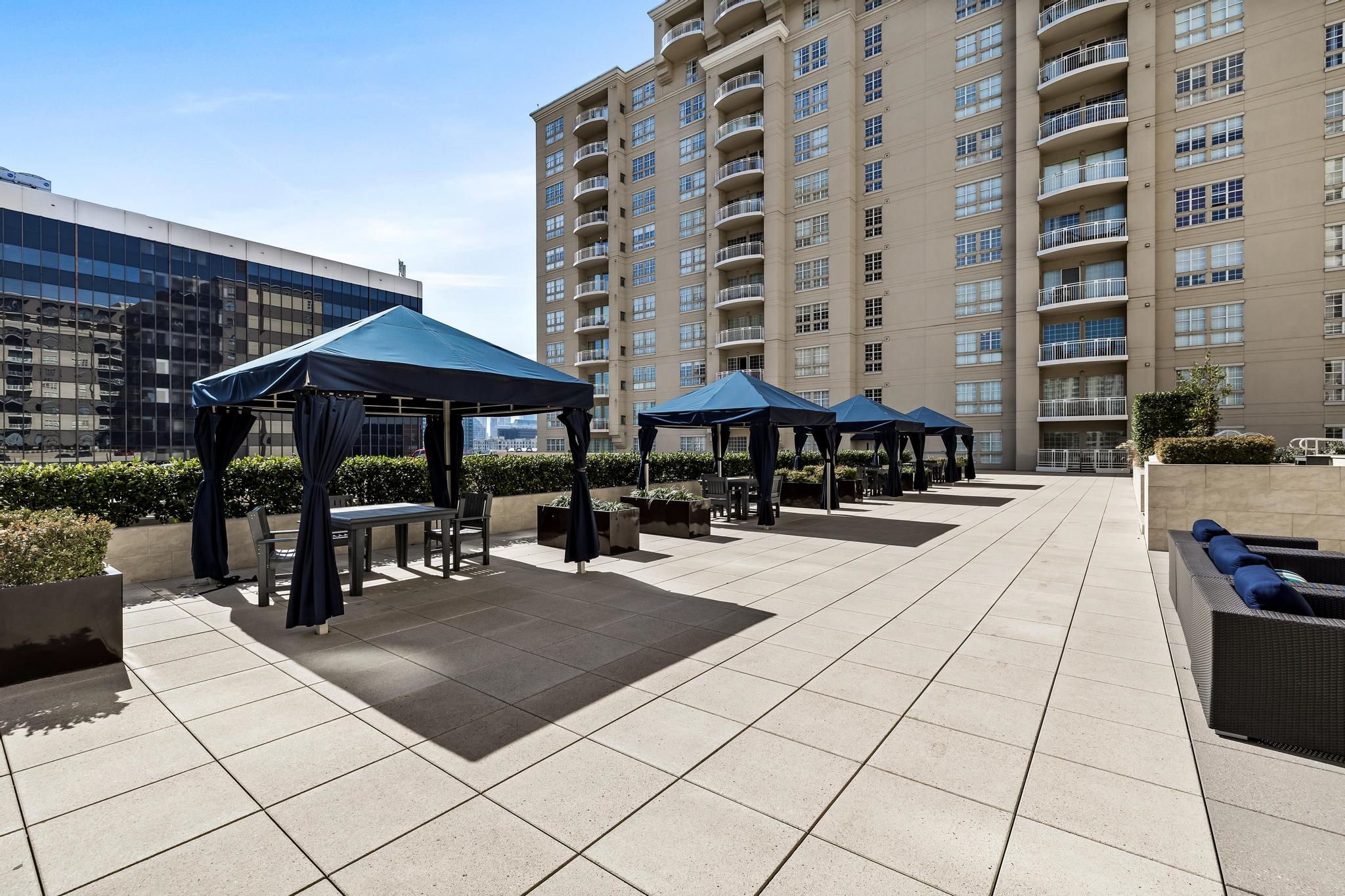Rooftop terrace with navy canopy tents, outdoor tables, planters, and lounge seating beside a high-rise building.