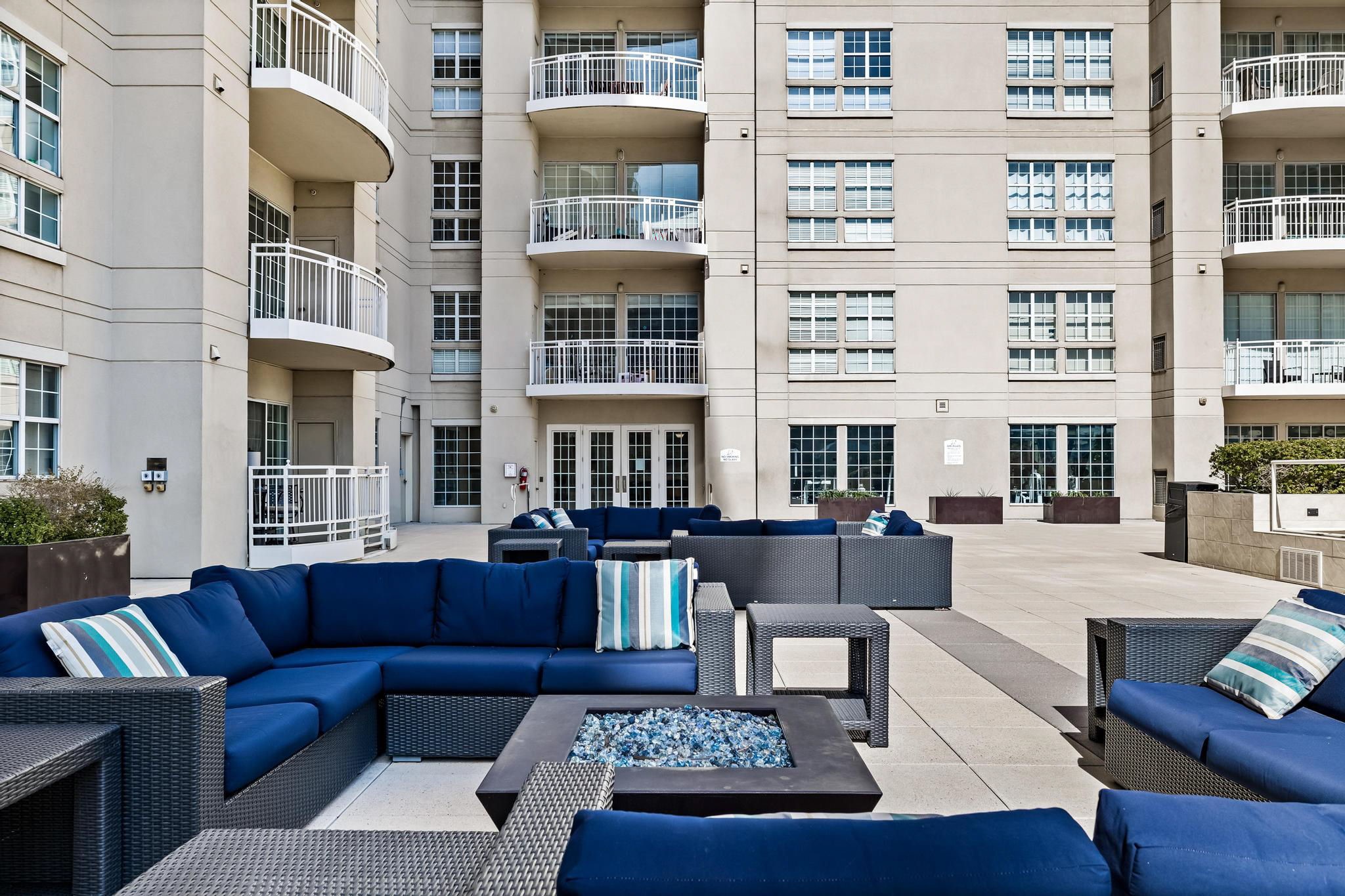 Condominium courtyard with blue outdoor sofas surrounding a fire pit and balconies behind them