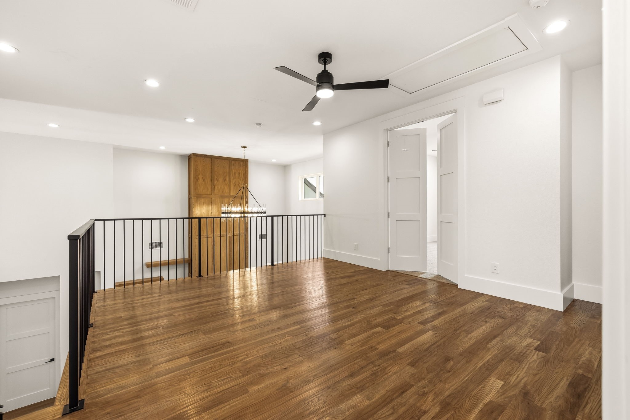 Upstairs landing with wood floors, a black railing, built-in cabinet, chandelier, and ceiling fan.