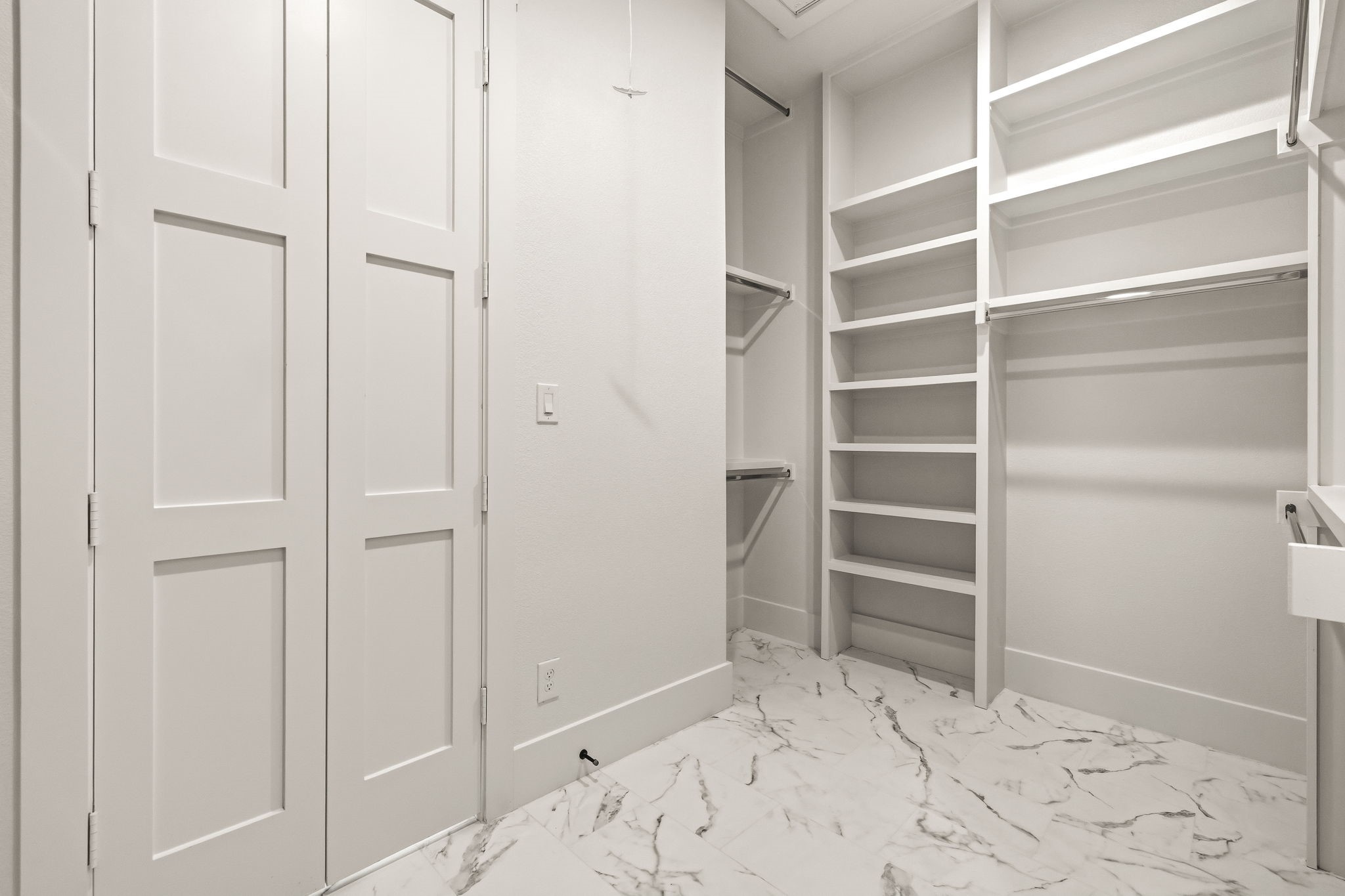 Walk-in closet with built-in white shelving and hanging rods over marble-look tile flooring.