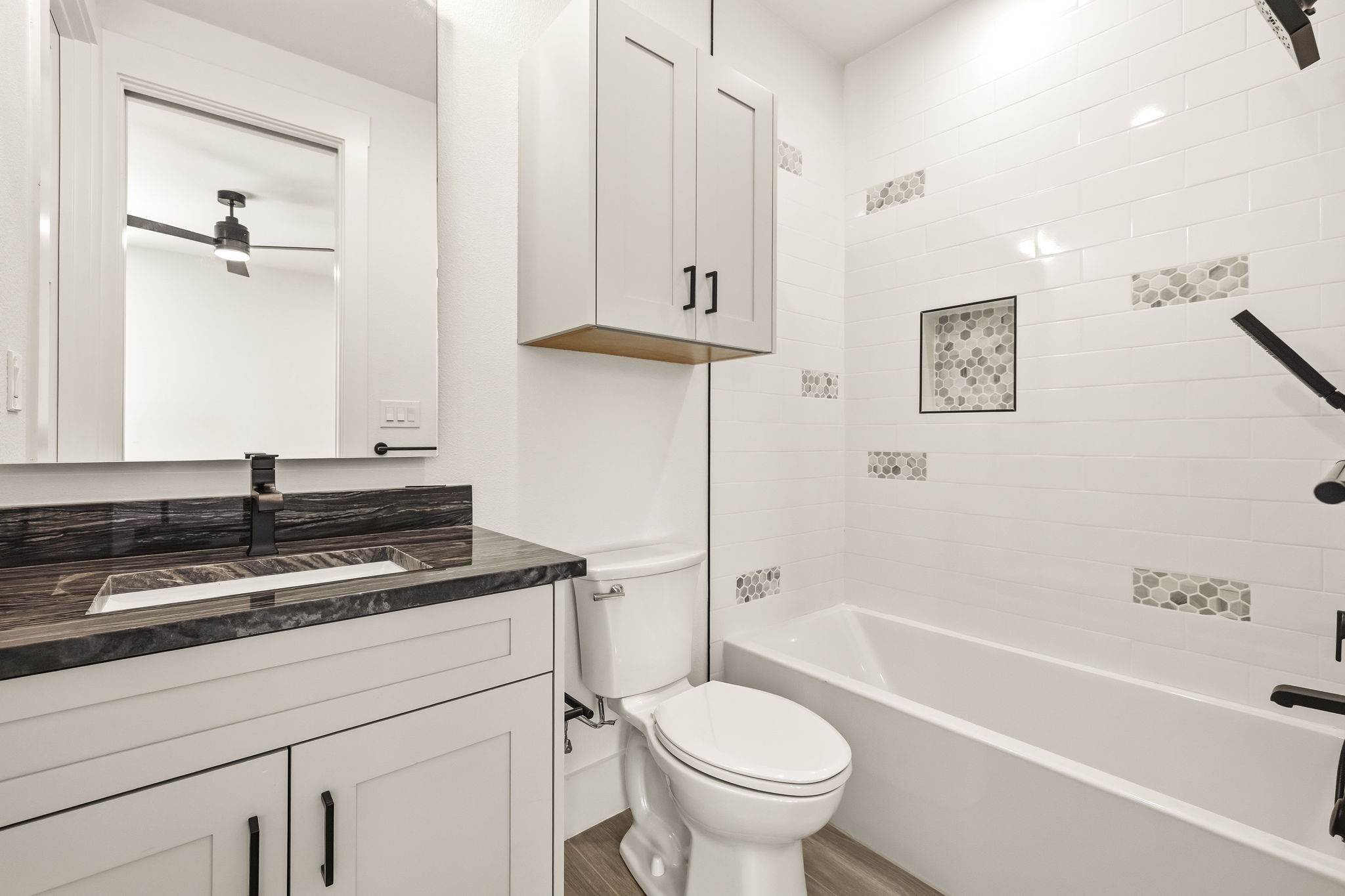Bathroom with a white subway-tile tub surround, gray hexagon accents, and a dark stone vanity.