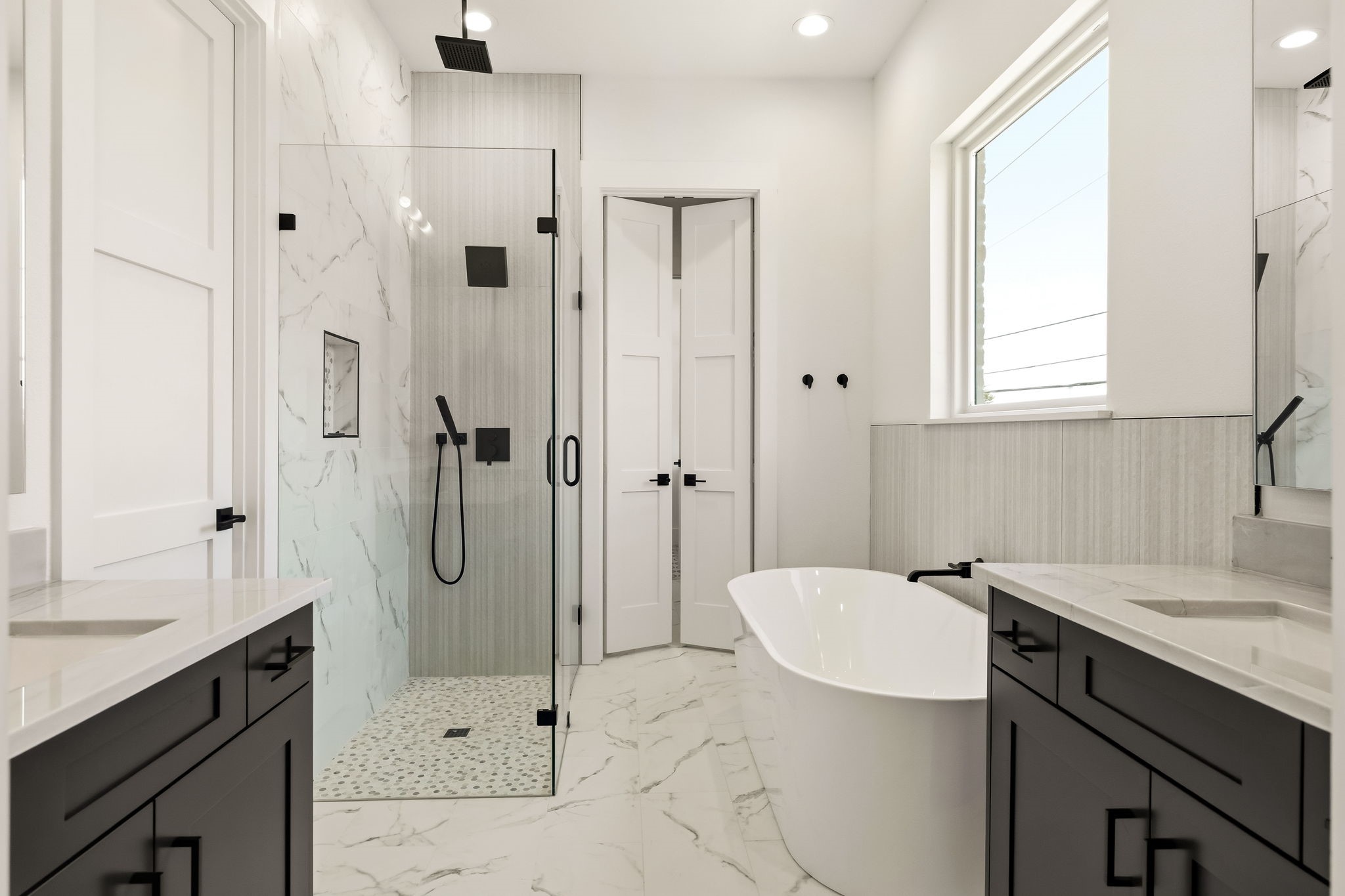 Modern bathroom with a glass walk-in shower, freestanding soaking tub, and dark double vanities.