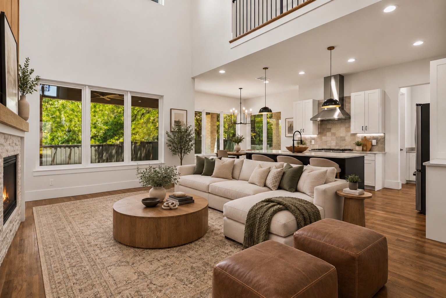 Open-plan living room and kitchen with a vaulted ceiling, large windows, white sectional, and fireplace.