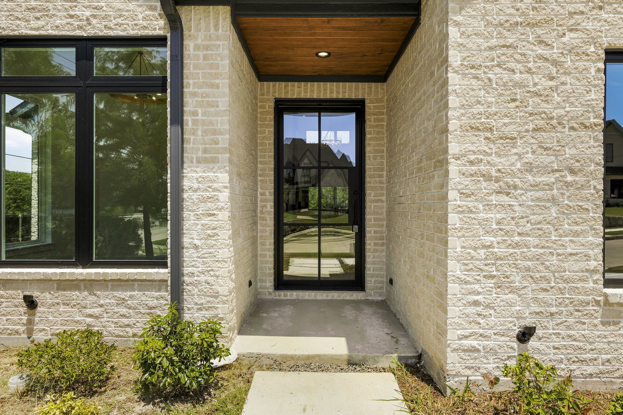Stone house entry with a black-framed glass door beneath a wood-paneled porch ceiling.