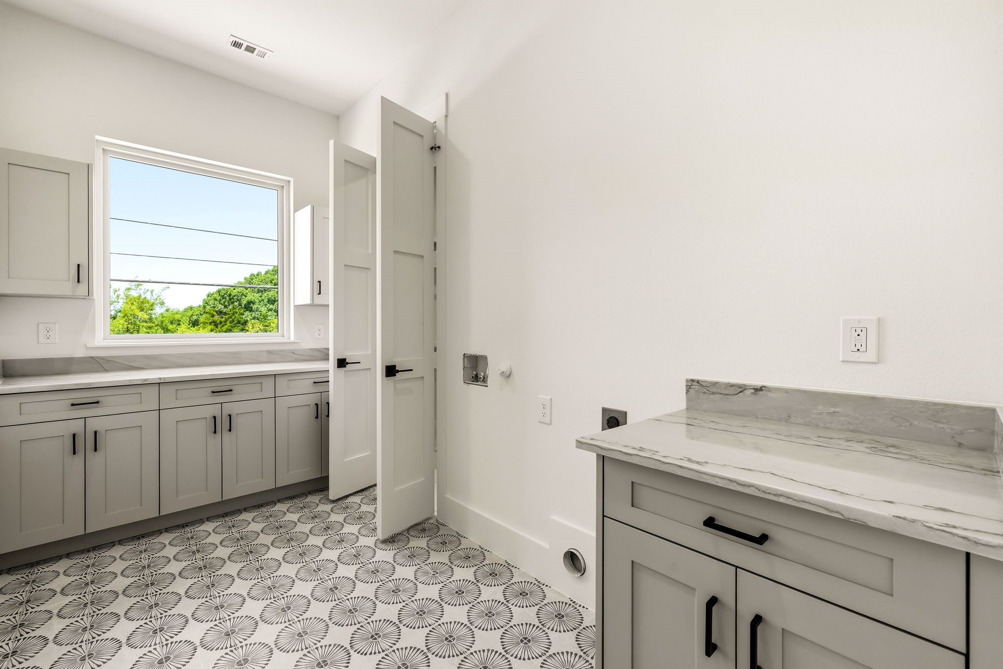 Laundry room with gray cabinets, stone countertops, a large window, and patterned tile floor.