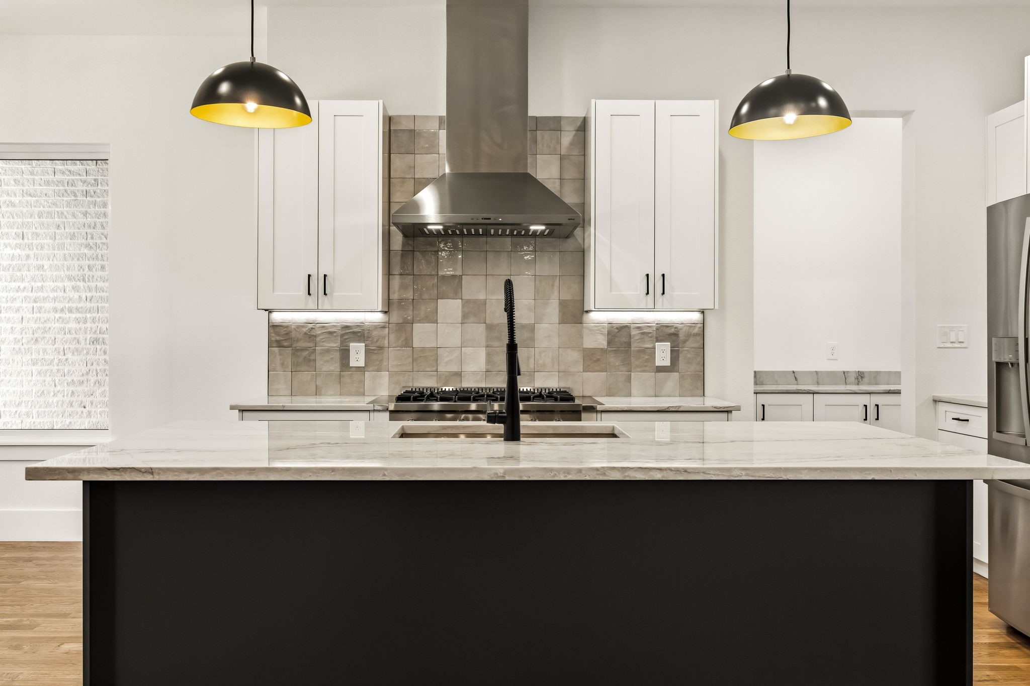 Modern kitchen with a marble island, tiled backsplash, gas cooktop, and stainless steel range hood.