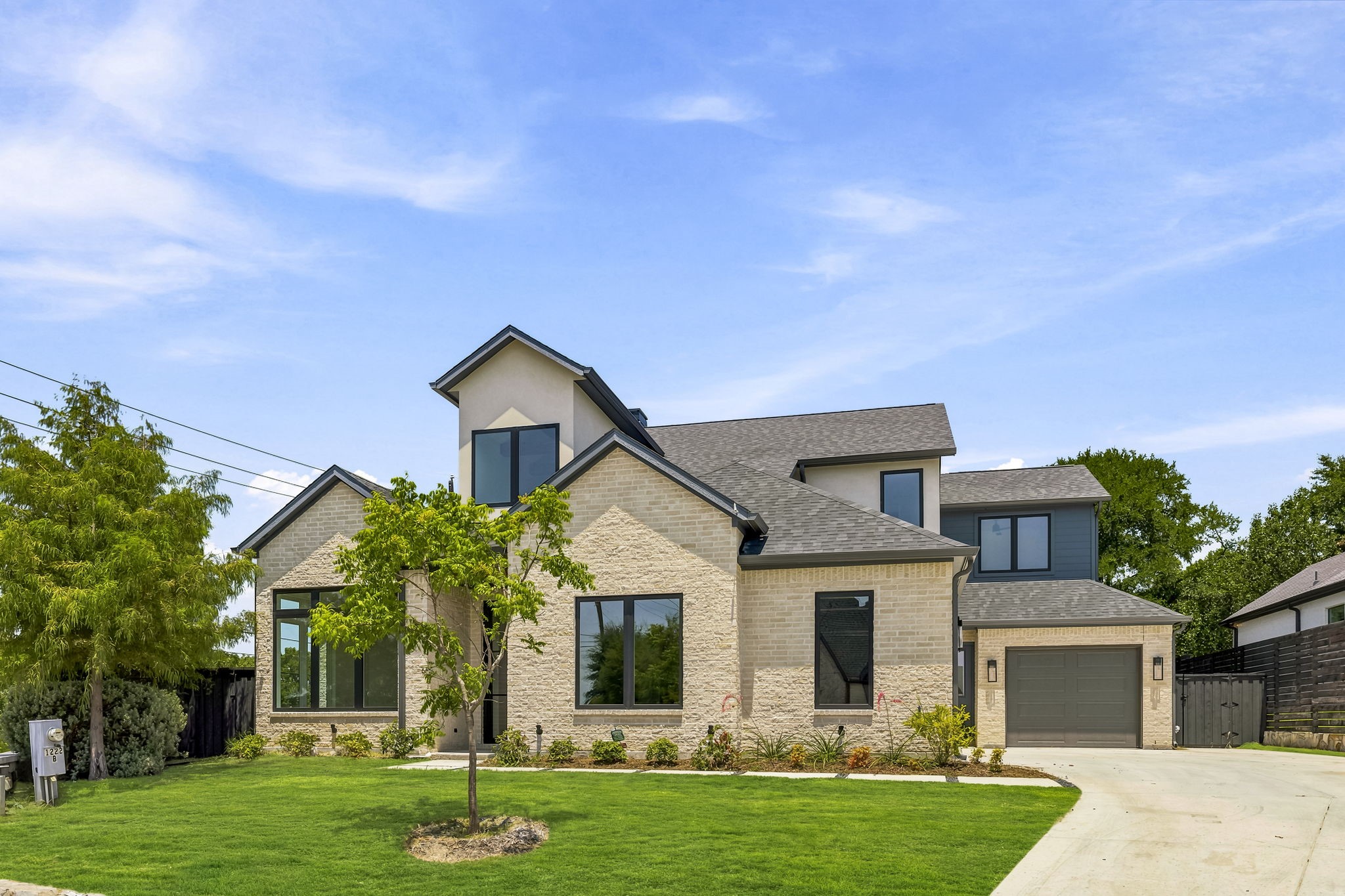 Multi-level stone home with dark-framed windows, attached garage, and landscaped front lawn.