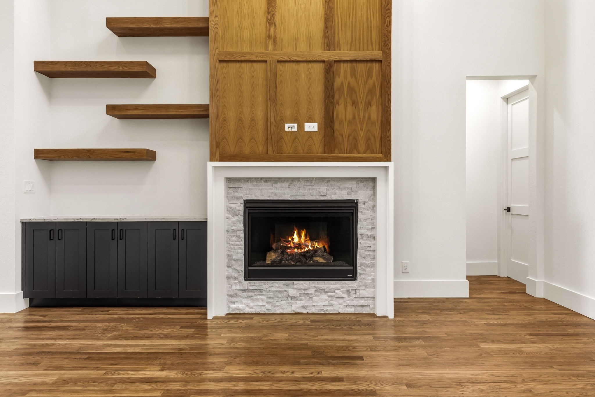 Living room with a stone fireplace, wood paneling, floating shelves, and dark built-in cabinets.