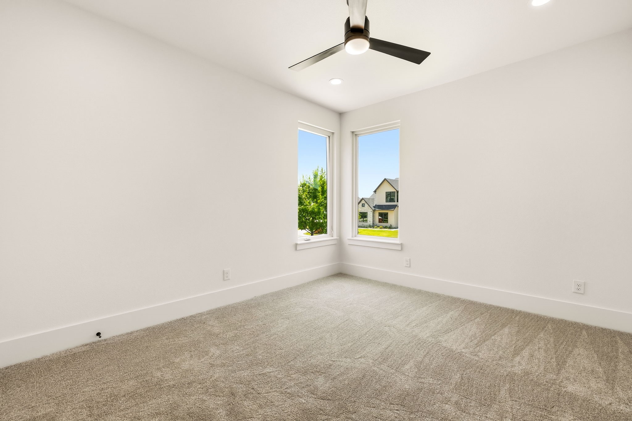 Empty bedroom with beige carpet, ceiling fan, and two corner windows.