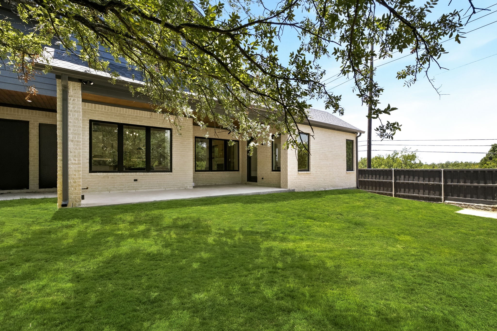 Light-brick home with a covered patio and large windows overlooking a broad lawn.