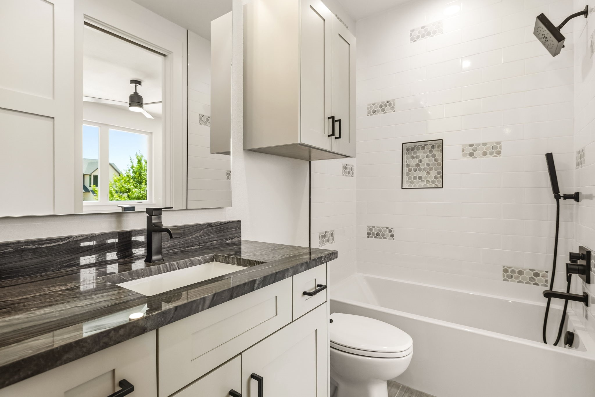 Modern bathroom with a dark stone vanity, black fixtures, and a white tub with hexagonal tile accents.