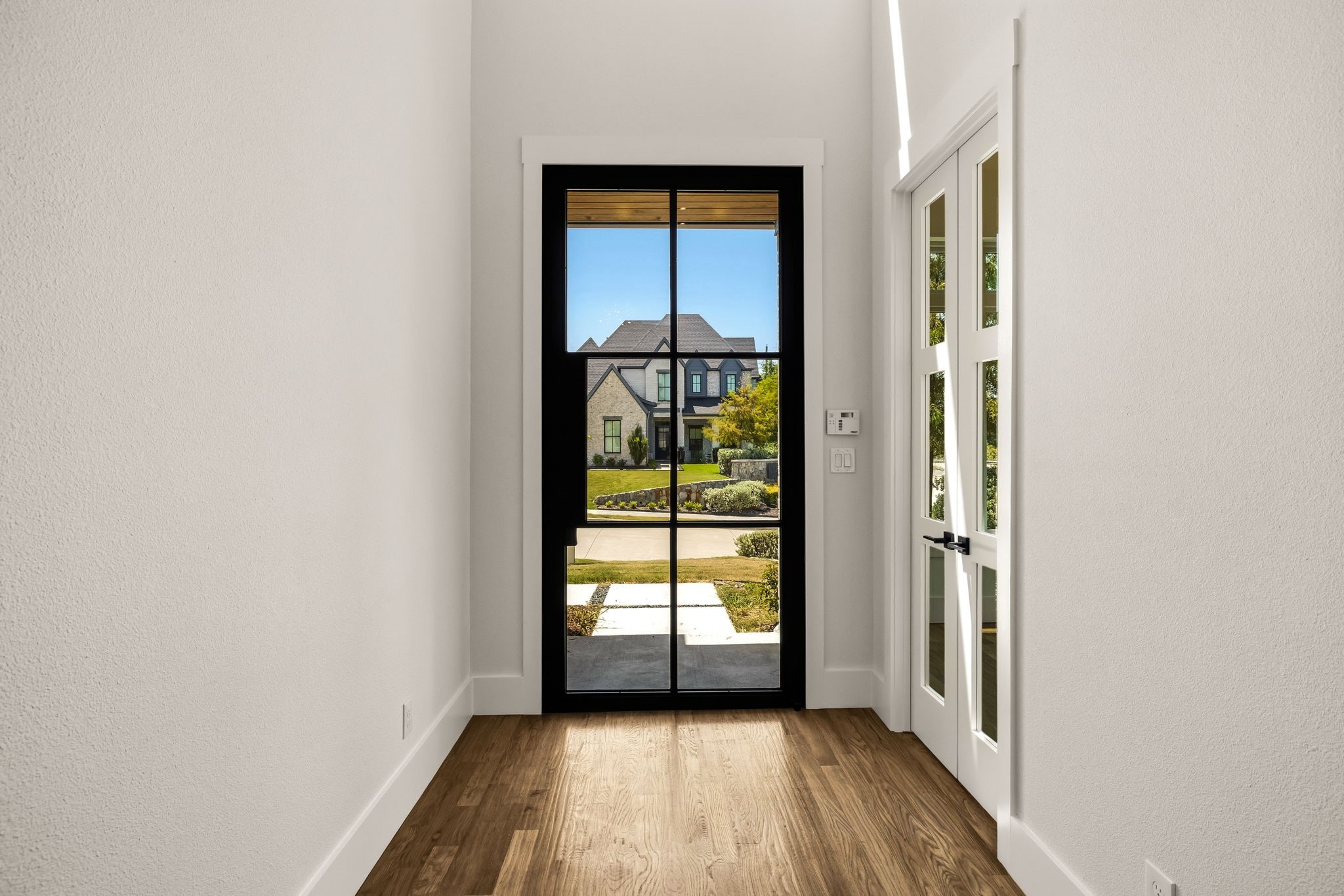 Unfurnished entryway with warm wood floors and a black-framed glass front door overlooking the yard.