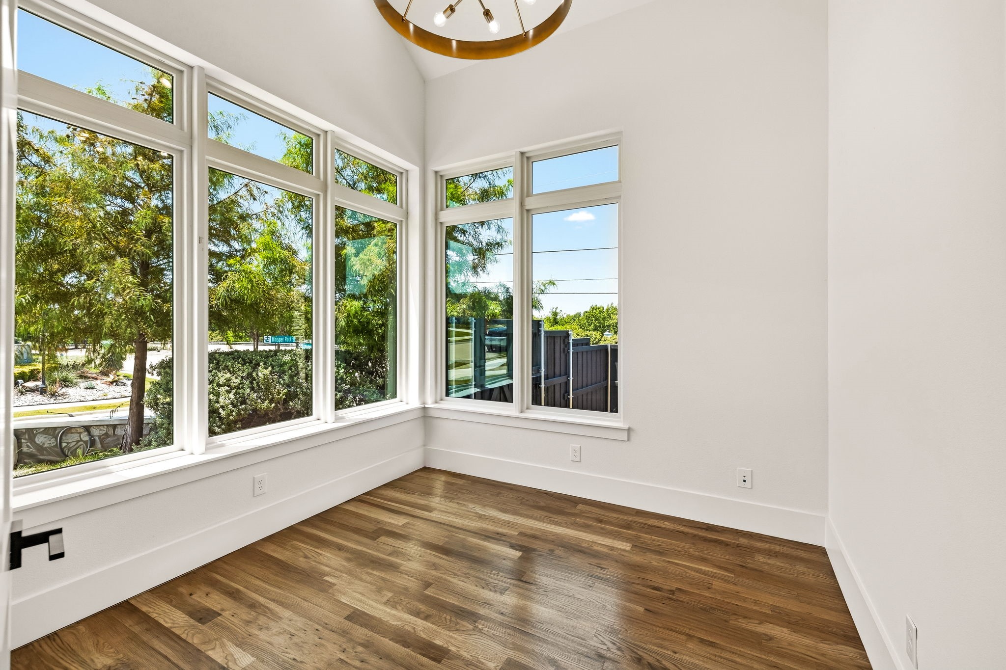 Bright empty room with expansive corner windows, a high ceiling, and wood flooring.