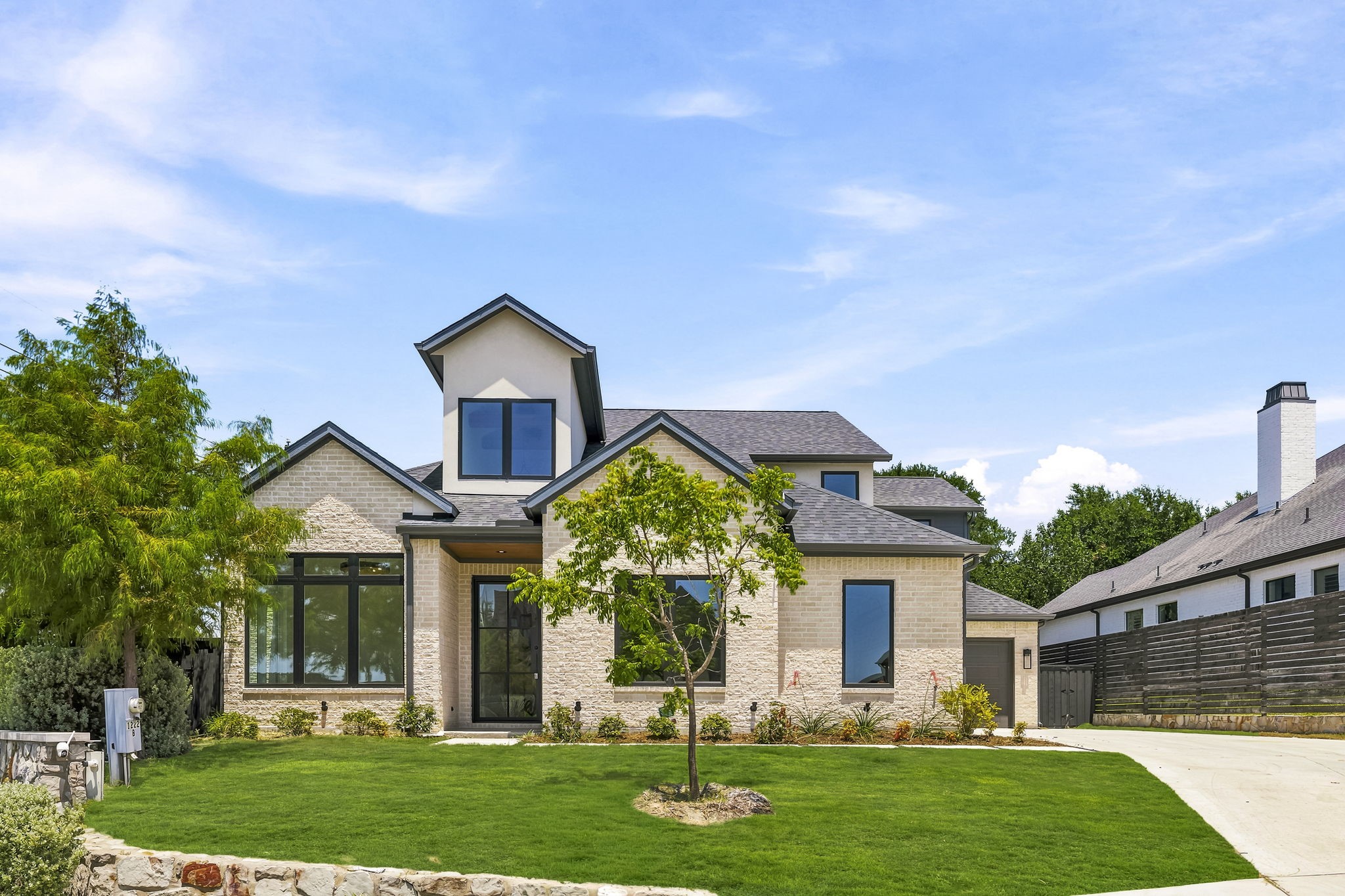 Two-story stone-and-stucco home with dark-framed windows, a broad lawn, and a driveway.